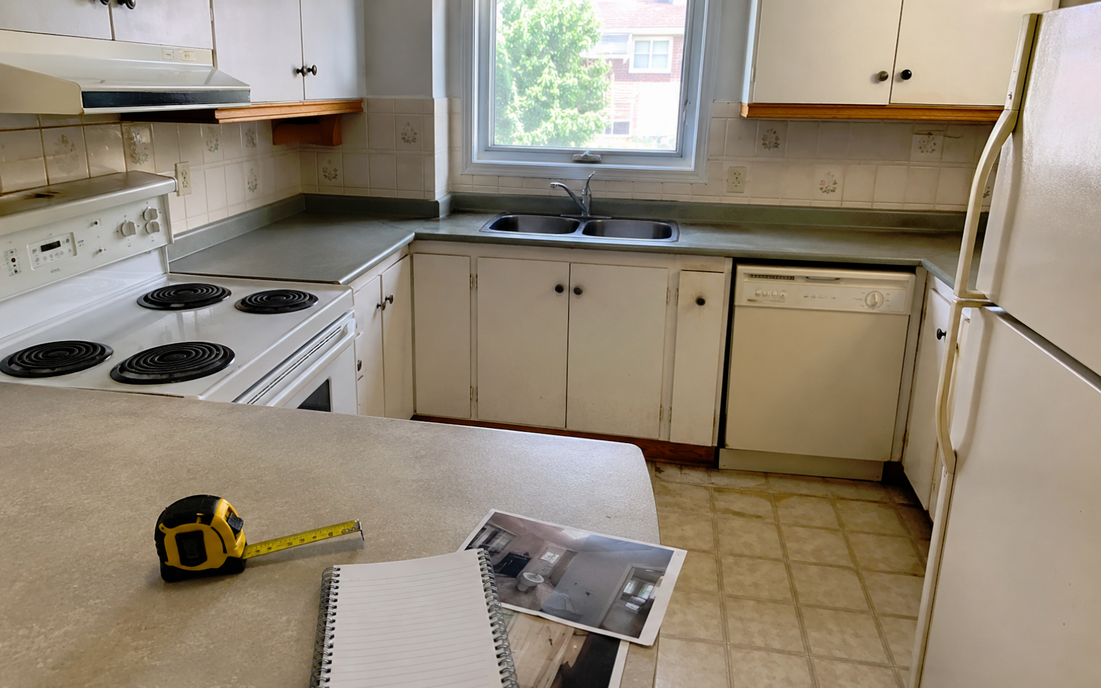 Existing kitchen condition review in a Toronto home with outdated cabinets, measuring tape, notebook, and renovation photos before an estimate