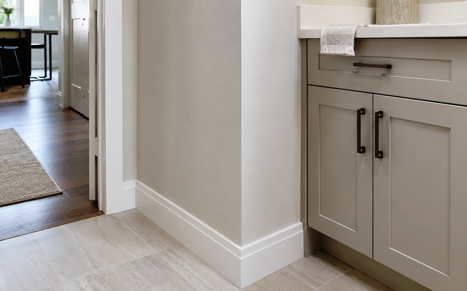 Interior finish detail in a Toronto home showing painted wall, baseboard, trim, cabinetry edge, and clean transition between tile and wood flooring